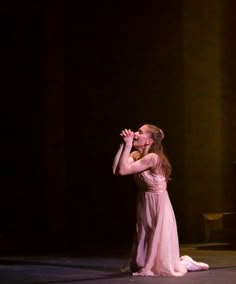 a woman in a pink dress standing on stage with her hand up to her mouth