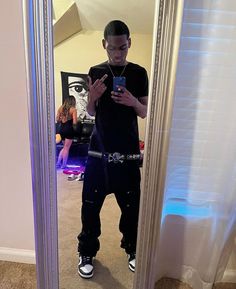 a young man standing in front of a mirror looking at his cell phone and taking a selfie