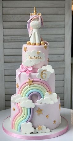 a three tiered cake decorated with unicorns and rainbows is on top of a table