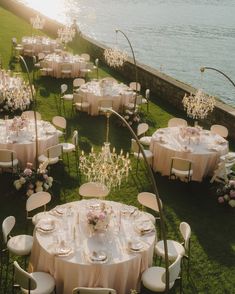 tables and chairs are set up on the lawn by the water for a formal dinner