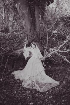 an old photo of a woman in a white dress and veil standing next to a tree