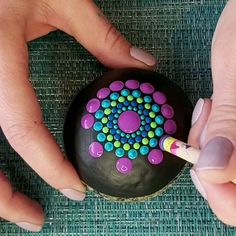 two hands are holding a painted rock with a pencil in it and another hand is drawing something on the rock