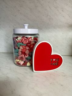 a jar filled with candy sitting on top of a counter next to a heart shaped container