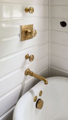 a bath tub sitting next to a white wall with gold faucets on it