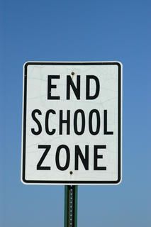 a white sign that says end school zone on the side of a road in front of a blue sky