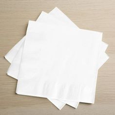 four white napkins are stacked on top of each other in front of a wooden table