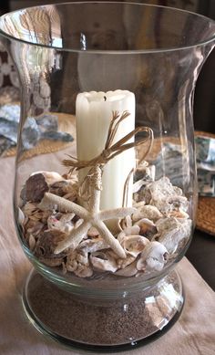 a glass vase filled with shells and a lit candle