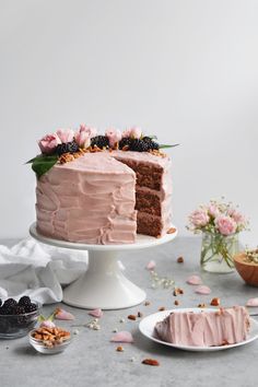 a cake with pink frosting and flowers on the top is surrounded by other desserts