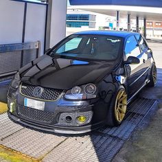 a black car parked in front of a gas station with yellow rims on it