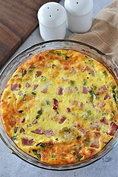 an omelet with ham, cheese and spinach in a glass dish next to two candles