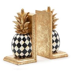 two black and white pineapples sitting next to each other in front of a gold bookend