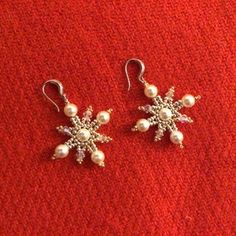 two pairs of earrings with pearls and snowflakes on them sitting on a red surface