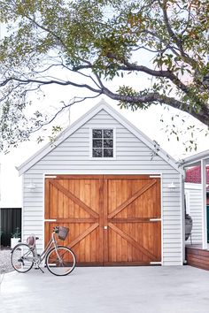 a bicycle parked in front of a white building with a wooden garage door and window