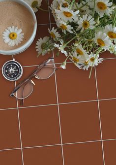 a cup of coffee and some daisies on a tile floor next to a compass