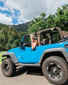 a woman sitting in the drivers seat of a blue jeep with her head out the window