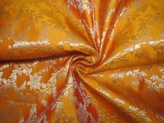 an orange and gold fabric with white flowers on the top, as well as leaves