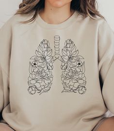 a woman sitting down wearing a sweatshirt with flowers on the chest and lungs drawn on it