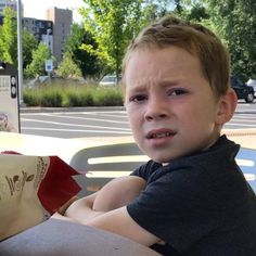 a young boy sitting at a table with a bag of chips in front of him