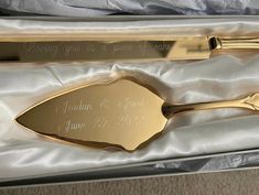 two gold colored serving utensils in a silver box with writing on the side