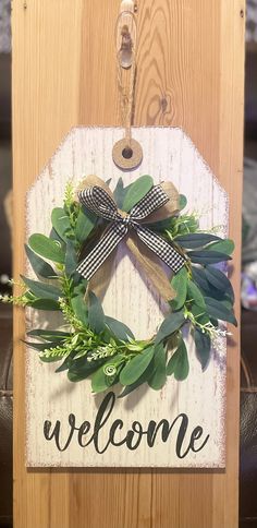 a welcome sign hanging on the side of a wooden door with a bow and greenery