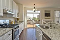 a kitchen with white cabinets and marble counter tops, along with an open door leading to the patio