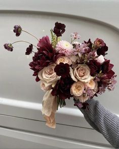 a bouquet of flowers is being held up by someone's hand in front of a car