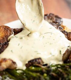 a white plate topped with asparagus and potatoes covered in ranch dressing being held by a spoon