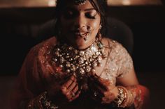 a woman in a bridal outfit with jewelry on her face and hands clasped together