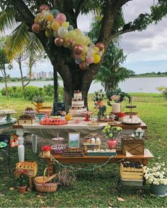 a table covered in lots of desserts under a tree with balloons hanging from it