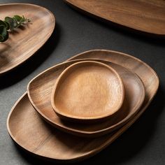 wooden plates and bowls are stacked on top of each other, with green plants in the middle