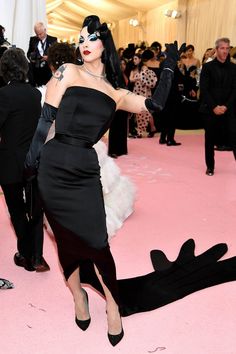 lady in black and white outfit walking on pink carpet with people behind her at an event