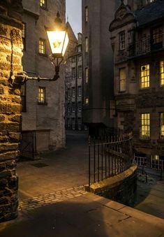 an old street light is lit up in the dark at night, with cobblestone streets and stone buildings surrounding it