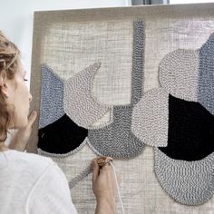 a woman working on a piece of art with yarn and thread in front of her