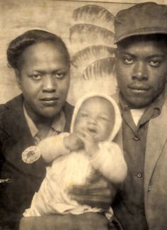 an old black and white photo of two men holding a baby in front of a painting