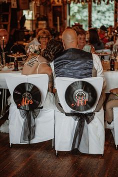 a man and woman sitting at a table with vinyl records on their backs, surrounded by other people