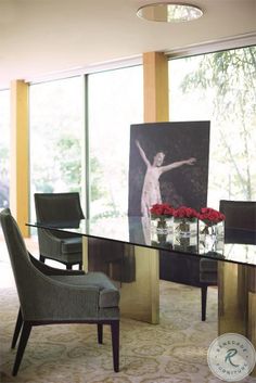 a glass table with chairs around it in front of a large window and painting on the wall