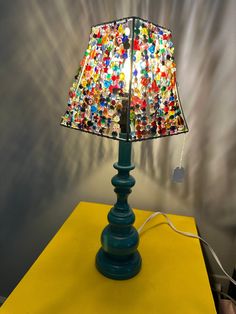 a lamp that is sitting on top of a yellow table with a colorful shade over it