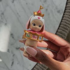 a hand holding a small doll with a crown on it's head