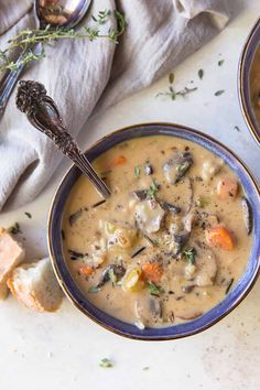 two bowls filled with soup and bread on top of a white tablecloth next to silver spoons