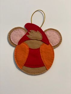 a felt mouse ornament hanging on a white wall with red and orange trim