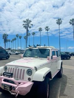 a pink and white jeep parked in a parking lot with palm trees on the other side