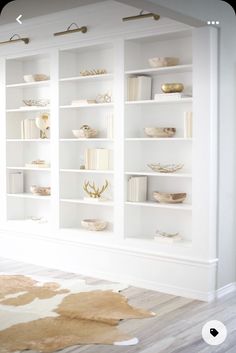 a living room with white bookcases filled with books and decorative items on top of them