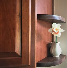 a white vase with an orange flower is sitting on a shelf in the corner of a cabinet