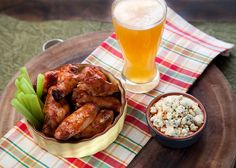 a wooden tray topped with chicken wings next to a bowl of celery and a glass of beer