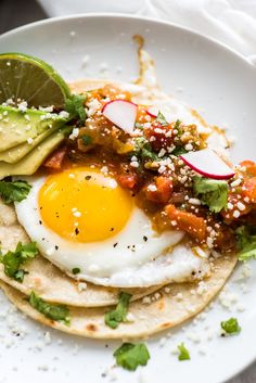 an egg is on top of some tortillas with avocado and cilantro