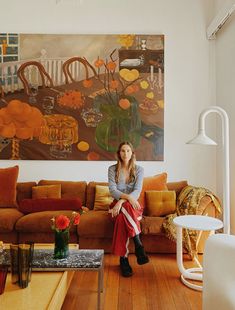 a woman sitting on top of a couch in a living room next to a painting