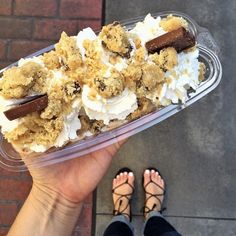 a person holding up a plastic container filled with ice cream and toppings on it