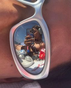 a woman taking a selfie in the reflection of her sunglasses while laying on the beach