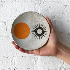 a hand holding a small bowl with an orange and black design on the side, against a white brick wall