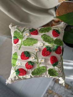 a pillow with strawberries and daisies is hanging from a hook on a wall